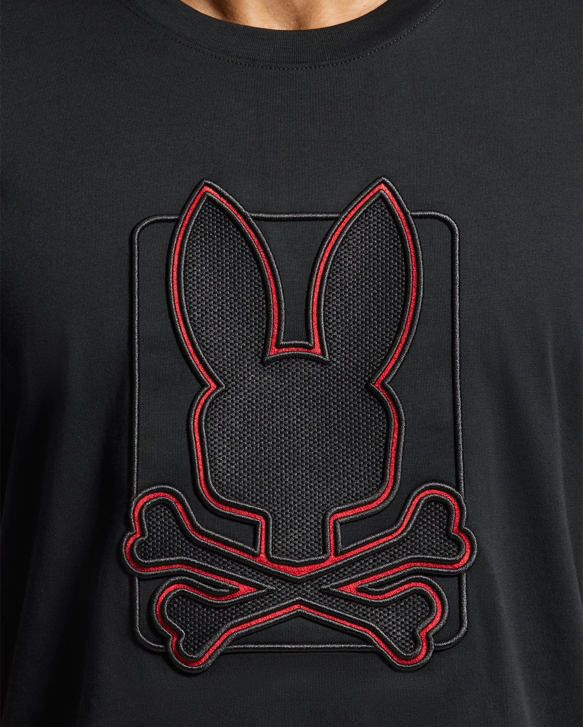 The Psycho Bunny MENS PIERCE EMBROIDERED GRAPHIC TEE - B6U115E200 is made from soft Pima cotton and features an eye-catching embroidered design of a black silhouette with bunny ears atop crossed bones. The bold red outline provides striking contrast, bringing the bunny embroidery to life against the sleek black fabric.