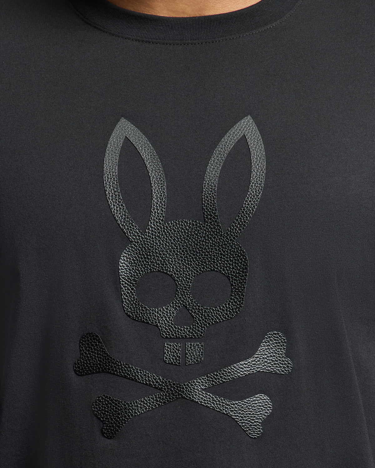 The Men's Payson Leather Print Graphic Tee from Psycho Bunny is crafted from soft Pima cotton jersey and features an embossed skull with bunny ears above crossed bones, echoing the classic pirate motif.