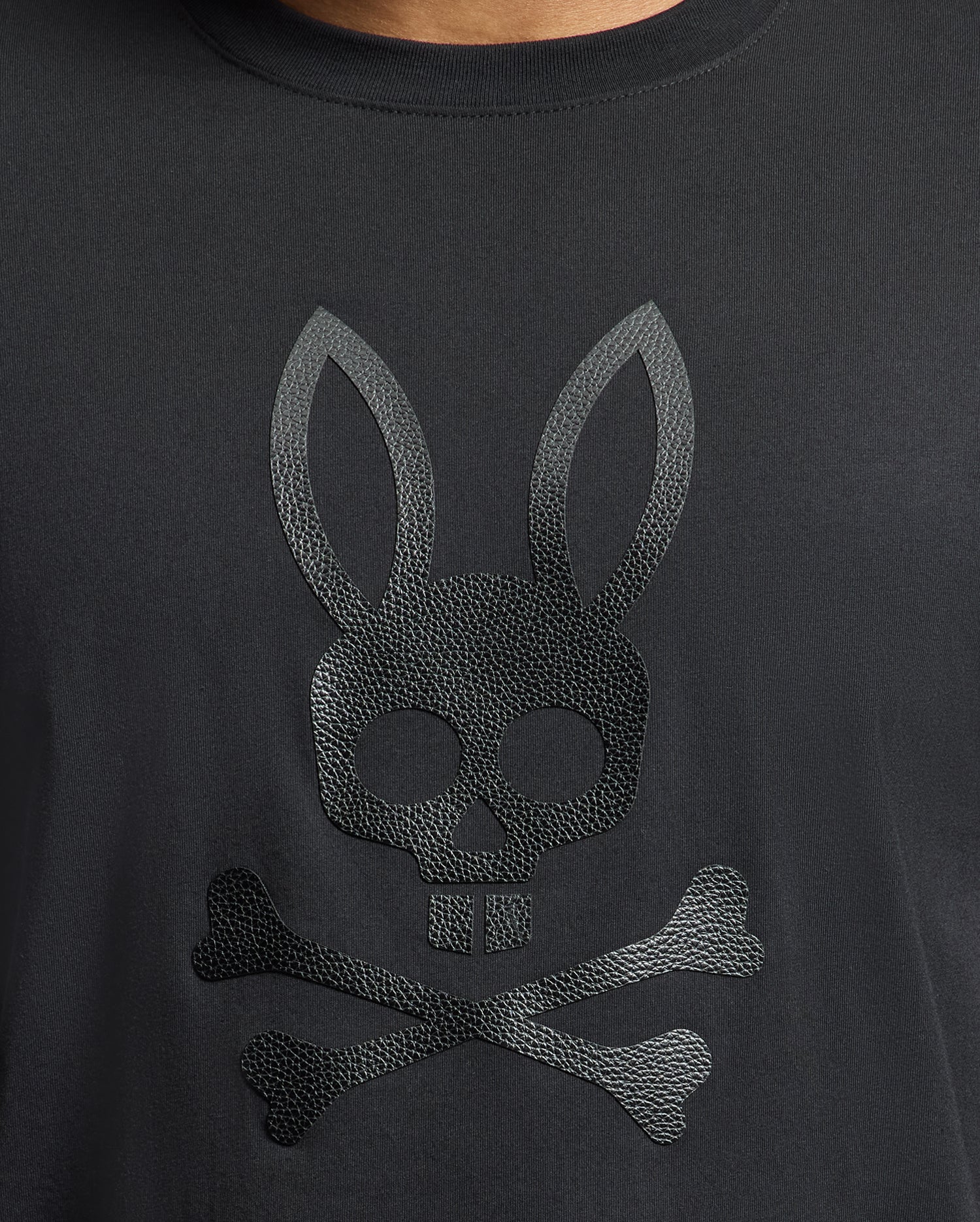The Men's Payson Leather Print Graphic Tee from Psycho Bunny is crafted from soft Pima cotton jersey and features an embossed skull with bunny ears above crossed bones, echoing the classic pirate motif.