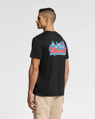 A man with short dark hair wears a black Psycho Bunny MENS MONTREAL TEE - B6U381F200 made of soft Pima cotton, showcasing "Montreal" and vibrant graphics on the back. His beige pants contrast against the plain white background.