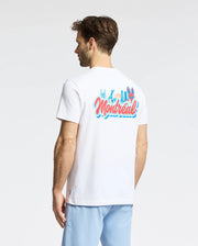 A man wearing the Psycho Bunny MENS MONTREAL TEE (B6U381F200), a white Pima cotton shirt with colorful "Montréal" text and a cartoon graphic on the back, stands facing away in light blue pants, displaying classic Psycho Bunny style.