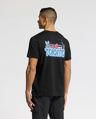 A man displays the MENS TORONTO TEE - B6U383F200 by Psycho Bunny, crafted in luxurious Pima cotton. The tee features vibrant graphics of iconic landmarks like a rabbit and the CN Tower on the back as he faces away from a plain background, highlighting his unique style.