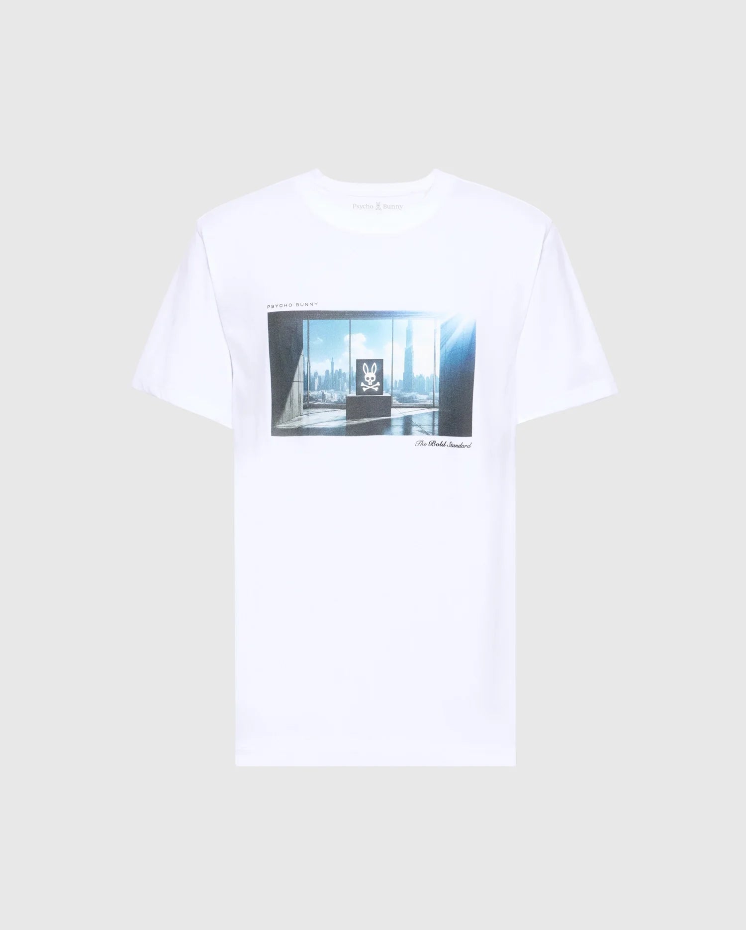 The MENS WARREN PHOTO REAL TEE by Psycho Bunny is a white Pima cotton T-shirt with a central graphic print of a city skyline through windows lit by sunlight, featuring illegible text.