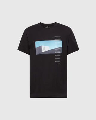 The Psycho Bunny MENS NEIL PHOTO REAL TEE (B6U389E200) is a black t-shirt made from ultra-soft Peruvian Pima cotton featuring a graphic with a blue rectangle, white emblem, and vertical text, inspired by brutalist structures.