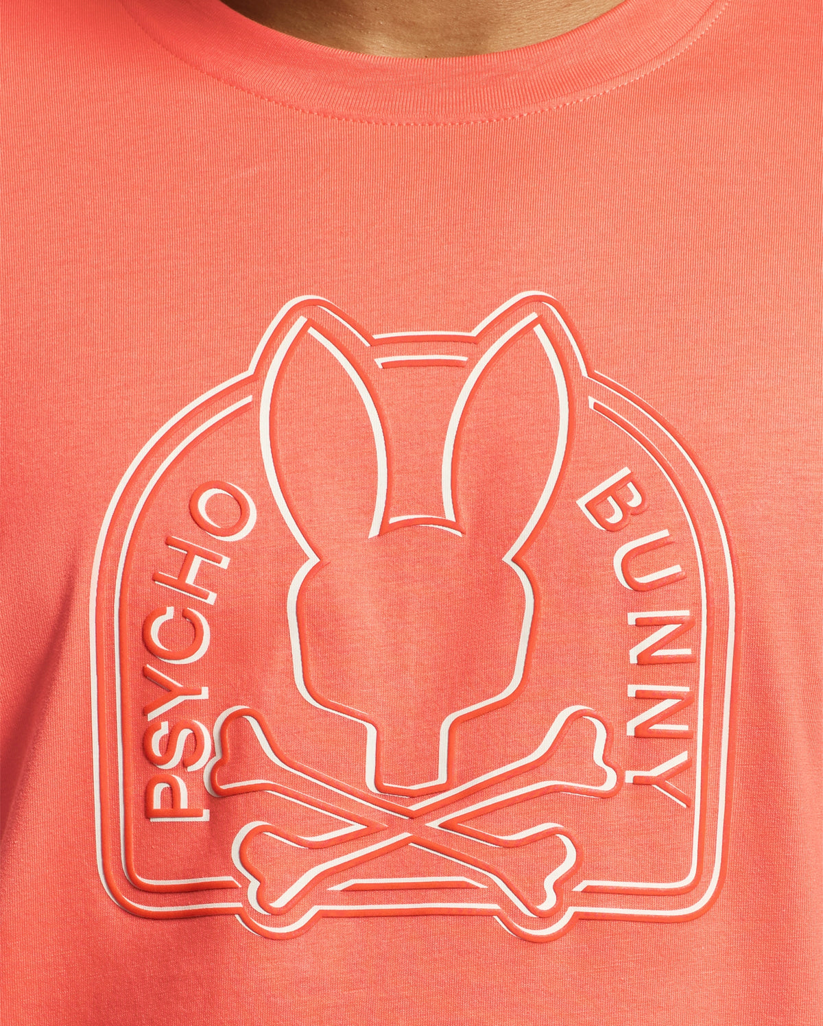 The Melbourne tee by Psycho Bunny, made from eco-friendly Pima Cotton in coral, features an embossed bunny head with crossbones design and "Psycho Bunny" printed on the sides.