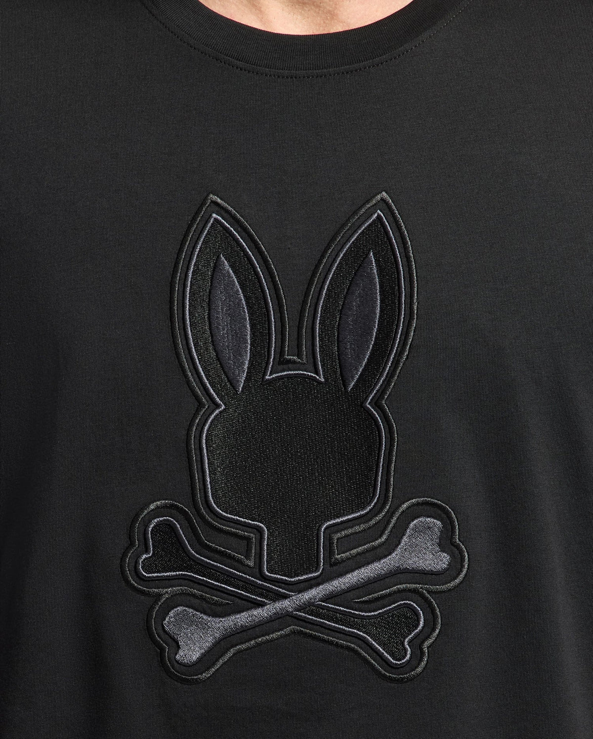 Close-up of the Psycho Bunny MENS NEW CASTLE EMBROIDERED GRAPHIC TEE in soft Pima cotton, featuring an embroidered bunny head with long ears above crossed bones, resembling a skull-and-crossbones design.