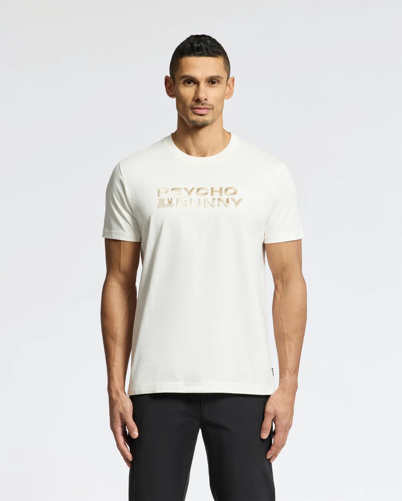 The man, with short dark hair and a neutral expression, stands against a plain white background wearing sleek black pants and the MENS BERNI EMBROIDERED WORDMARK GRAPHIC TEE - B6U417F200 by Psycho Bunny, featuring soft Pima cotton and a gold embroidered logo.