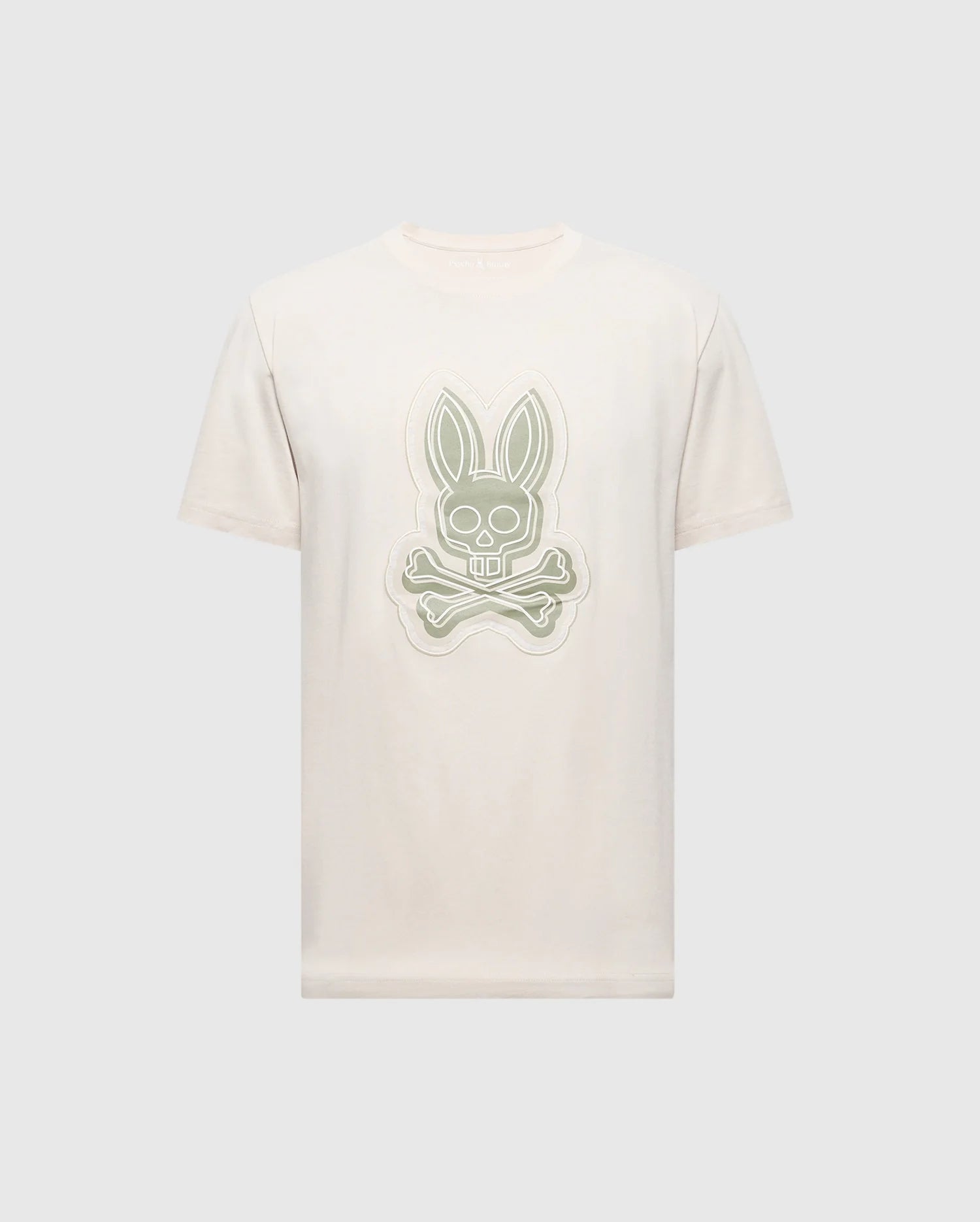 The MENS SYDNEY GRAPHIC TEE by Psycho Bunny, style B6U508F200, is a beige short-sleeve shirt made from soft Pima cotton. It features a bold central cartoon bunny graphic with crossbones beneath its head, strikingly standing out against the plain background.