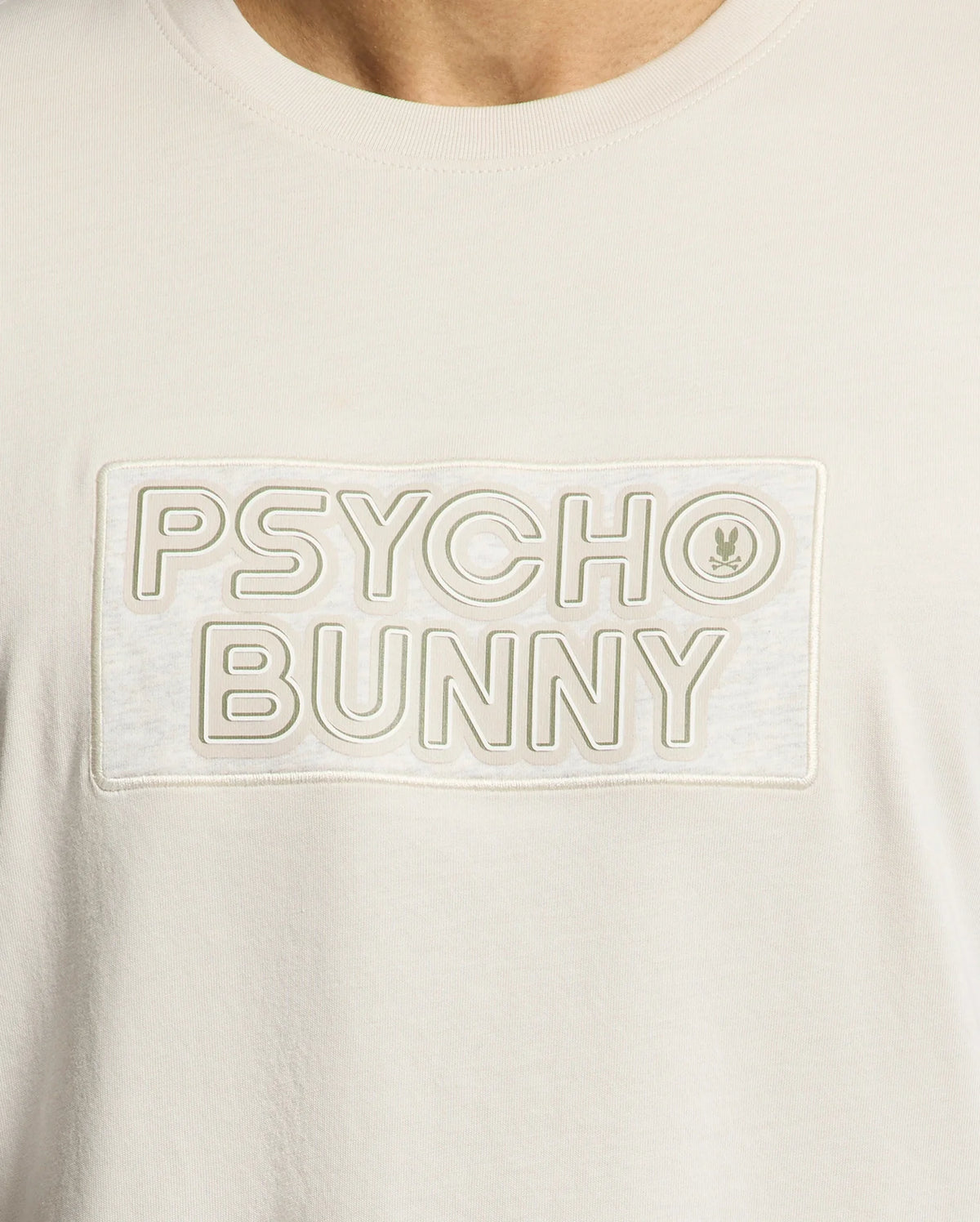 Close-up of the Psycho Bunny MENS SYDNEY WORDMARK GRAPHIC TEE (B6U510F200): light Pima cotton, "PSYCHO BUNNY" in large outlined letters across the chest, with a bunny logo in the "O" and a soft water-based print.