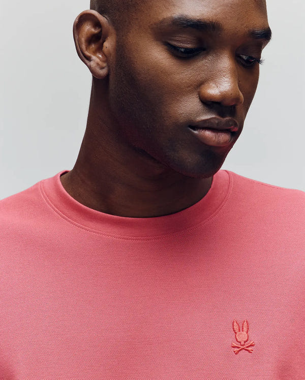 A man in a Psycho Bunny MENS TAYLOR PIQUE TEE (B6U579F200) with an embroidered bunny logo looks down neutrally, showcasing the shirt’s stylish silhouette against a plain background.