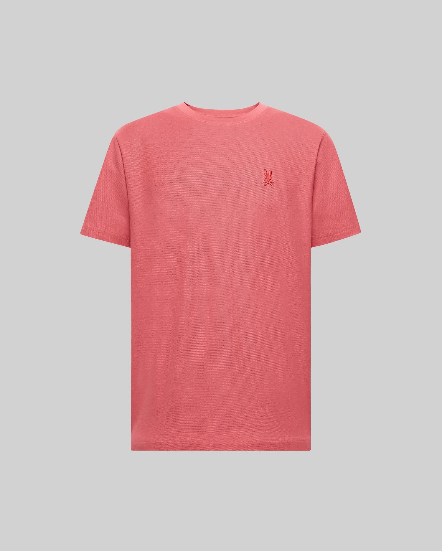 The Psycho Bunny MENS TAYLOR PIQUE TEE - B6U579F200 is a coral pink, short-sleeve Pima cotton t-shirt with a small embroidered logo on the left chest, shown against a light gray background.