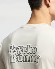 Back view of a person in the Psycho Bunny MENS ELLIOT FRONT BACK GRAPHIC TEE (B6U605F200), a light-colored, regular fit shirt featuring bold "Psycho Bunny" lettering across the upper back.