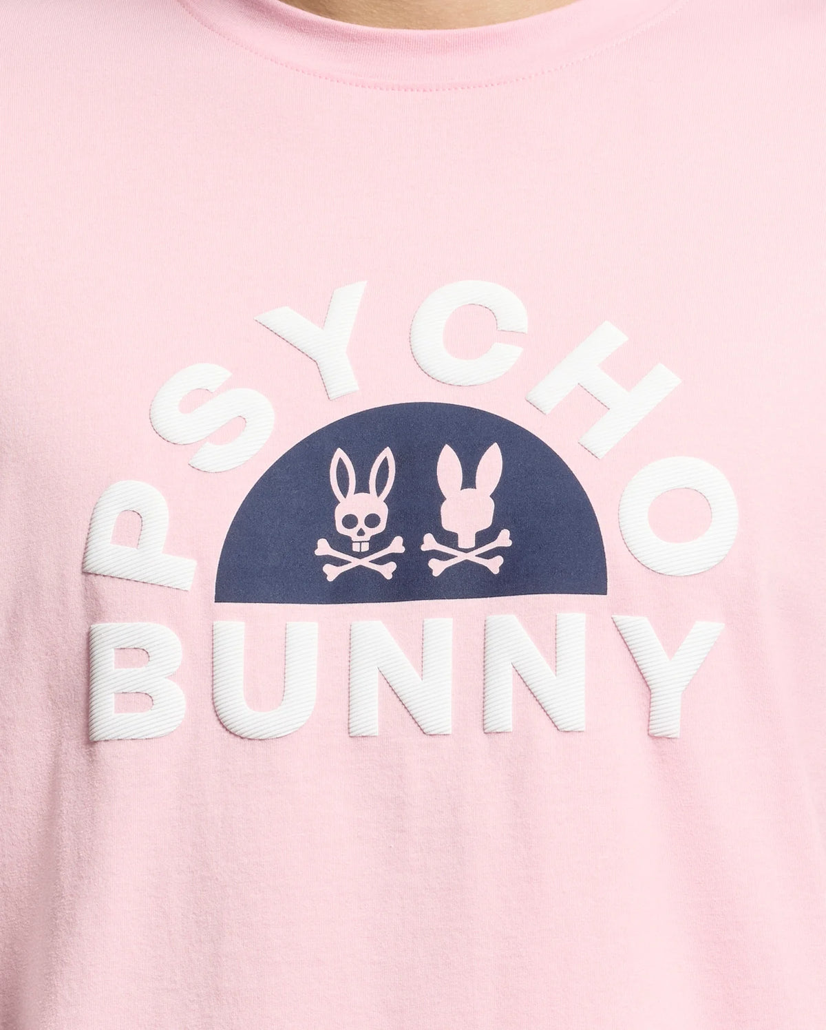 The MENS GOLDIE GRAPHIC TEE - B6U606F200 by Psycho Bunny is made from Peruvian Pima cotton. It features a pink color with navy bunny skull graphics above bold white "PSYCHO BUNNY" lettering.