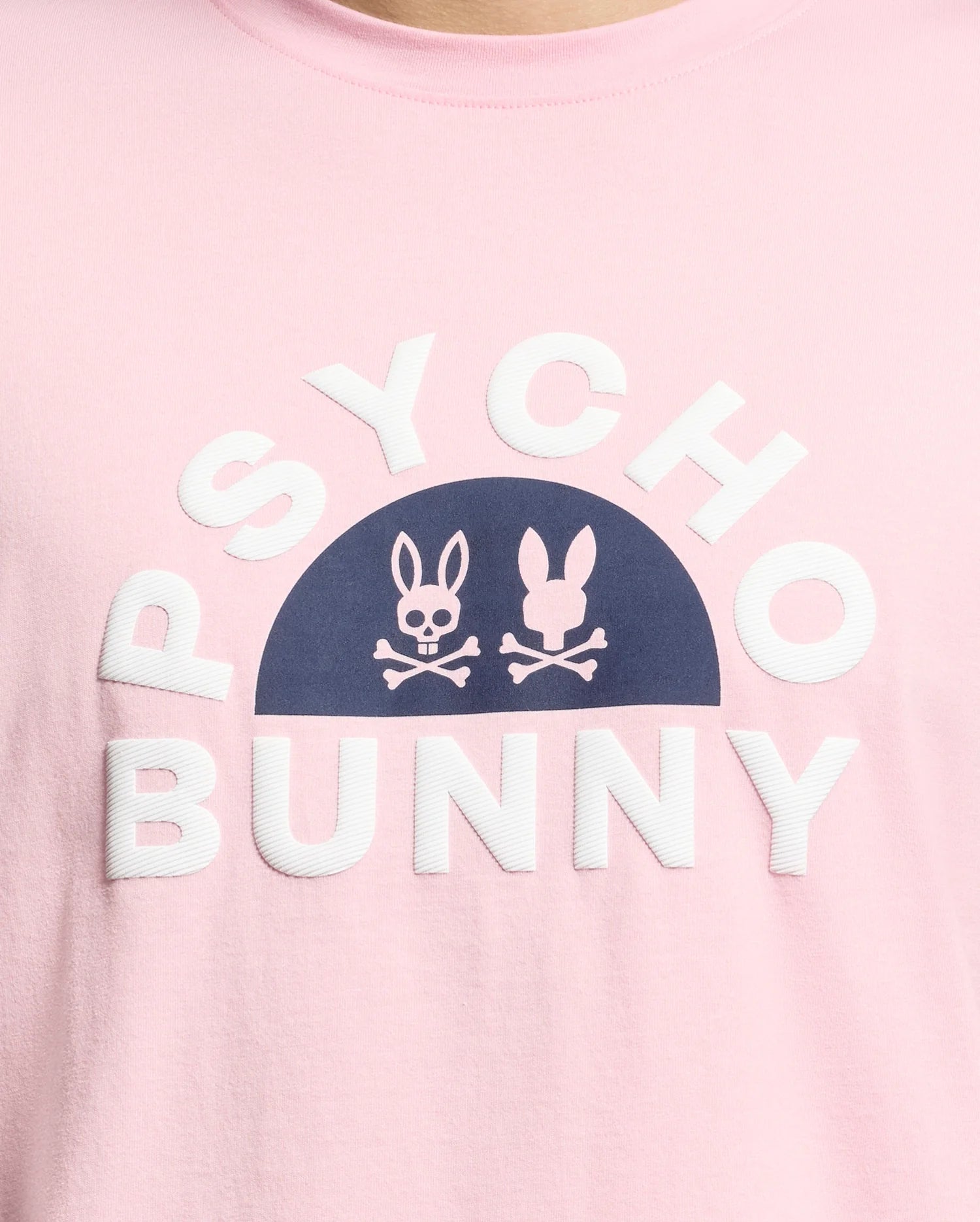 The MENS GOLDIE GRAPHIC TEE - B6U606F200 by Psycho Bunny is made from Peruvian Pima cotton. It features a pink color with navy bunny skull graphics above bold white "PSYCHO BUNNY" lettering.