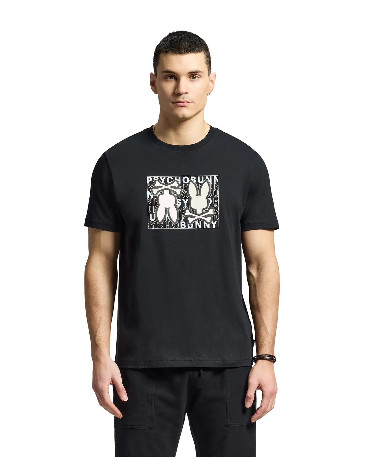 A man is wearing a Psycho Bunny "MENS GOLD COAST GRAPHIC TEE - B6U631F200" in black, made from premium Pima cotton. The classic fit shirt features a graphic bunny design, contrasting with a plain white background.