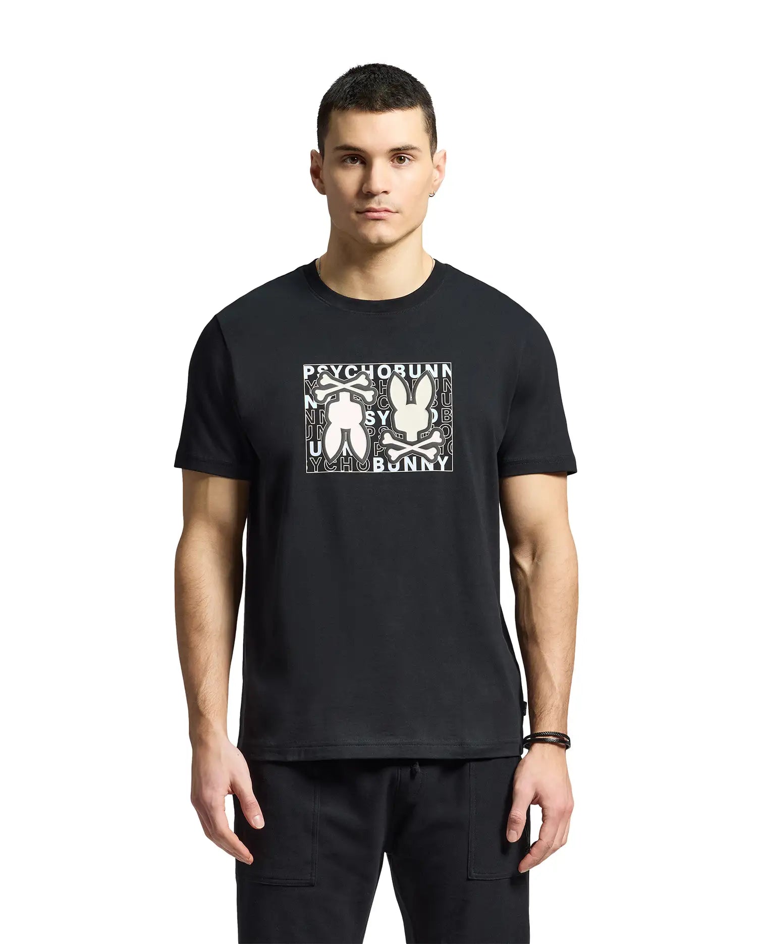 A man is wearing a Psycho Bunny "MENS GOLD COAST GRAPHIC TEE - B6U631F200" in black, made from premium Pima cotton. The classic fit shirt features a graphic bunny design, contrasting with a plain white background.