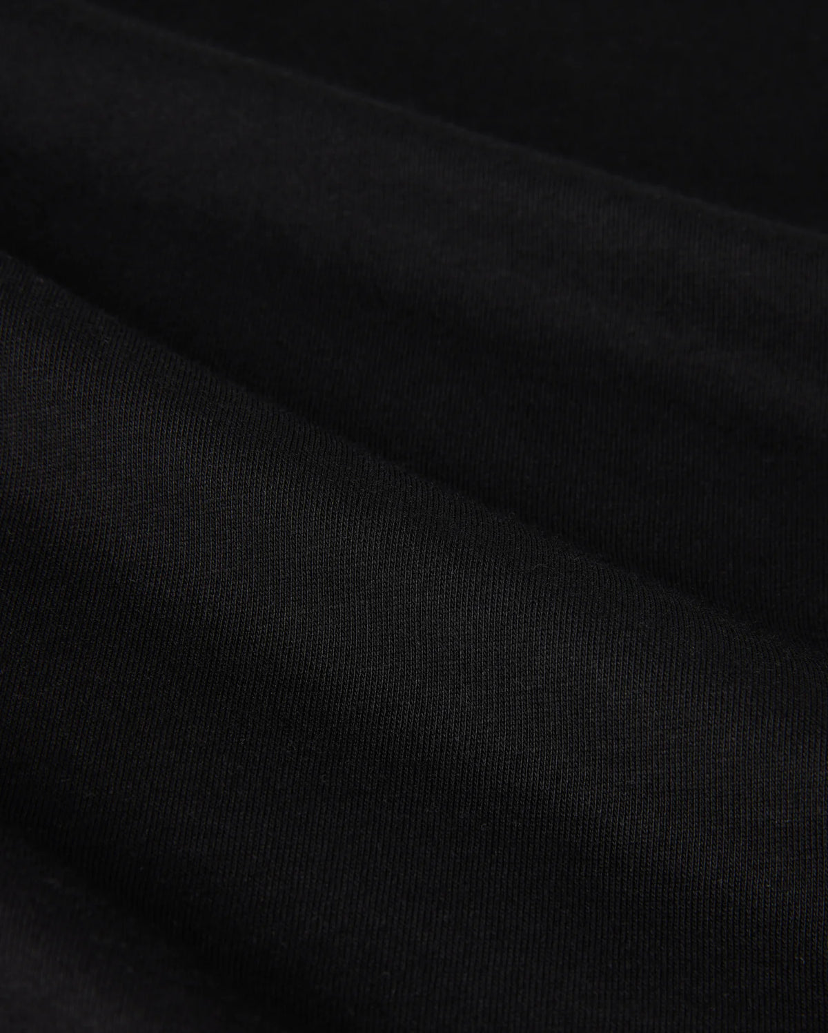 Close-up image of the MENS MELVIN GRAPHIC TEE - B6U663C200 by Psycho Bunny, showcasing its smooth, black Pima cotton fabric with a slightly textured surface. The tee is neatly folded, creating gentle, horizontal ridges and a subtle play of light and shadow.