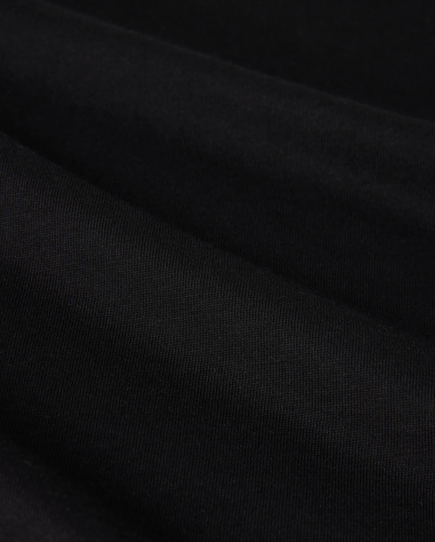 Close-up image of the MENS MELVIN GRAPHIC TEE - B6U663C200 by Psycho Bunny, showcasing its smooth, black Pima cotton fabric with a slightly textured surface. The tee is neatly folded, creating gentle, horizontal ridges and a subtle play of light and shadow.