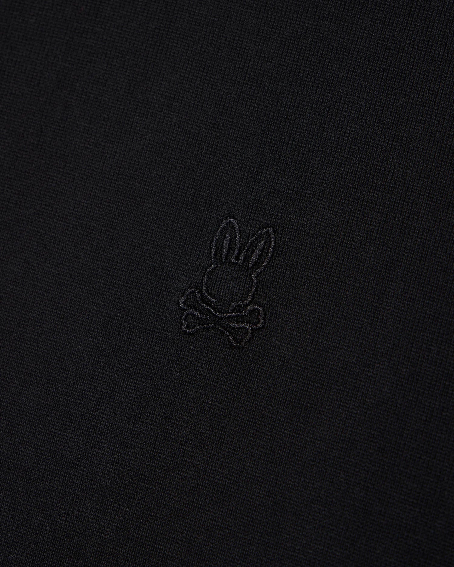 A close-up image of Psycho Bunny's MENS DUKE OVERSIZED TEE - B6U742D200, made from heavyweight Pima cotton fabric featuring an embossed rabbit head with long ears positioned above a pair of crossed bones. The subtle design blends slightly with the fabric, providing a relaxed and comfortable fit.