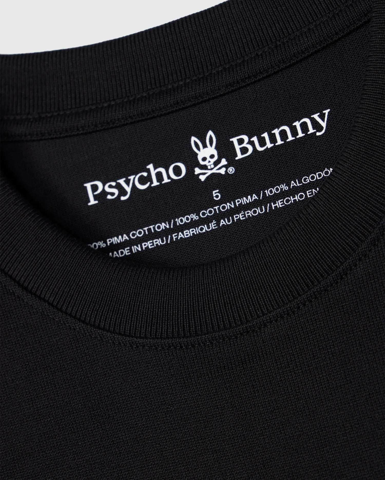 Close-up of the neckline and inner clothing label of a black MENS DUKE OVERSIZED TEE - B6U742D200 from Psycho Bunny. The label shows the brand name and logo, detailing "100% heavyweight Pima cotton," "Made in Peru," and featuring an embroidered chest bunny on this relaxed fit design.