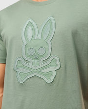 Product Name: MENS MALTON GRAPHIC TEE - B6U795D200
Brand Name: Psycho Bunny

Close-up of a person wearing the Psycho Bunny MENS MALTON GRAPHIC TEE - B6U795D200 in light green Pima cotton, featuring a stylized bunny skull and crossbones design prominently embossed in the center. This graphic tee combines style and comfort with its soft fabric, making it an essential addition to any wardrobe. Made in Peru.