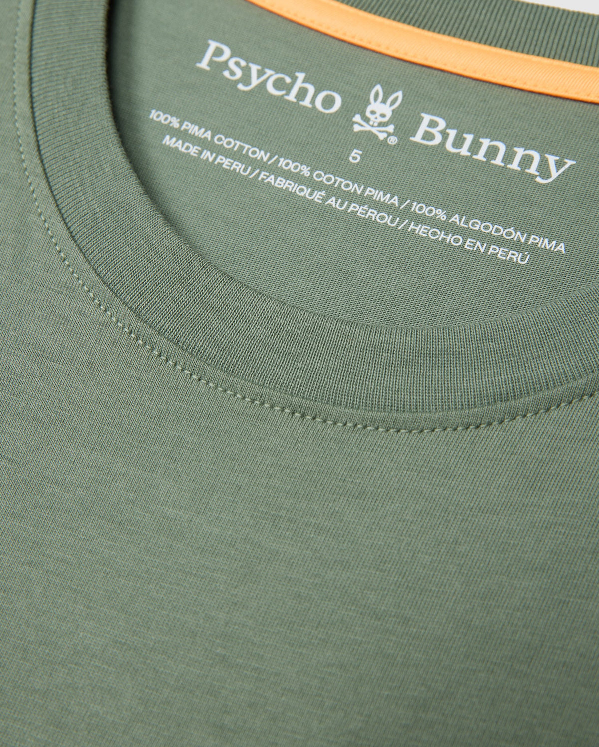 Close-up of the collar and neckline area of the MENS MALTON GRAPHIC TEE - B6U795D200 in green by Psycho Bunny. The shirt has a small printed label displaying the brand name, logo, size, and material composition — 100% Pima Cotton, Made in Peru. An orange strip is visible inside the collar seam.