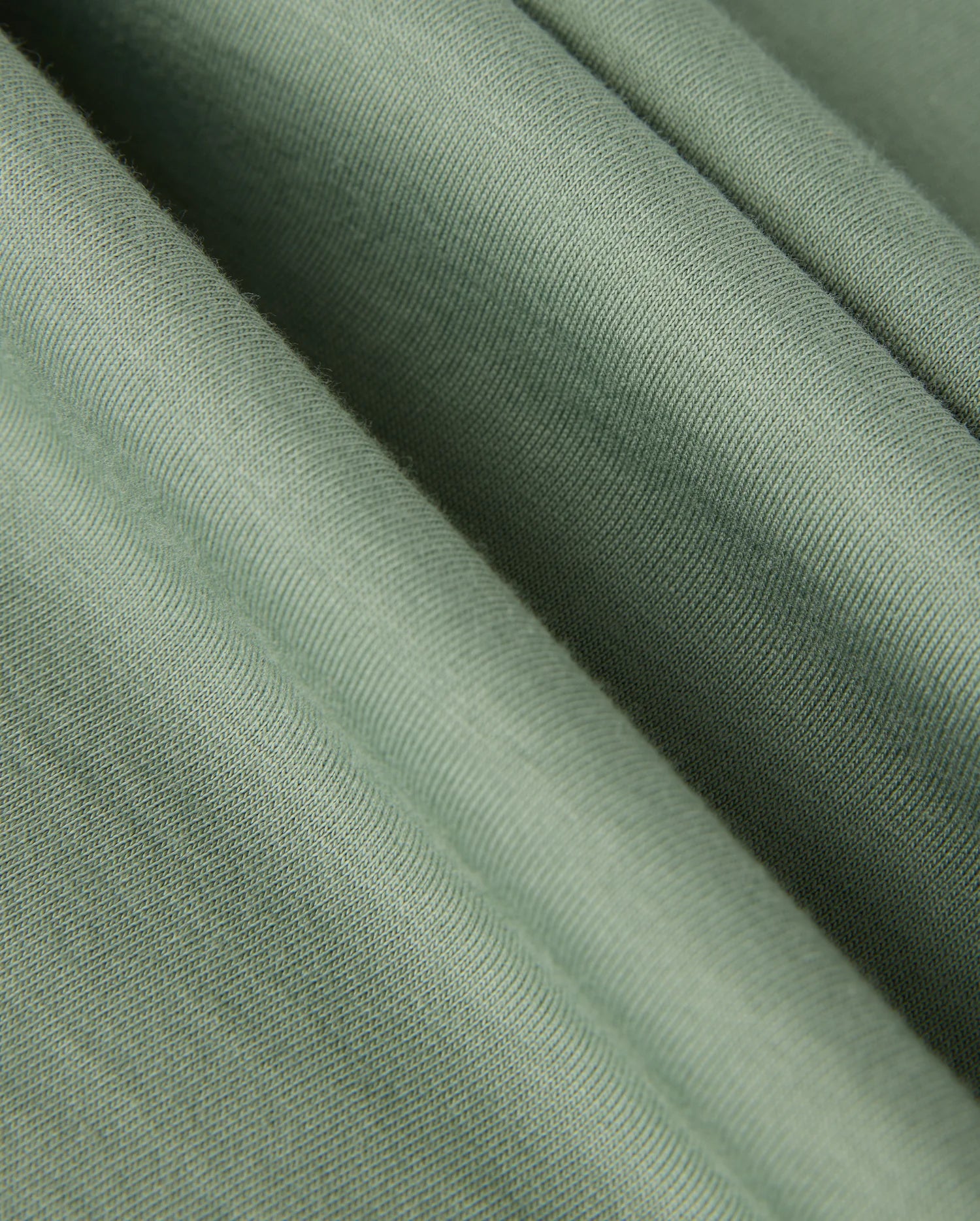 Close-up of a soft, light green fabric with visible ridges and folds. Made in Peru, the Pima cotton of the MENS MALTON GRAPHIC TEE - B6U795D200 from Psycho Bunny appears smooth and slightly textured, suggesting a comfortable and gentle material.