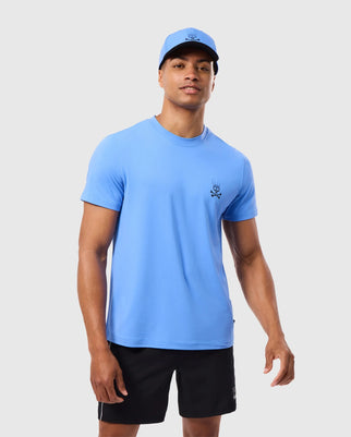 A person is dressed in a blue Psycho Bunny MENS MAXWELL SPORT BACK GRAPHIC TEE - B6U799D200 and a matching cap, both featuring breathable fabric and a small embroidered design, paired with black shorts against a plain white background.