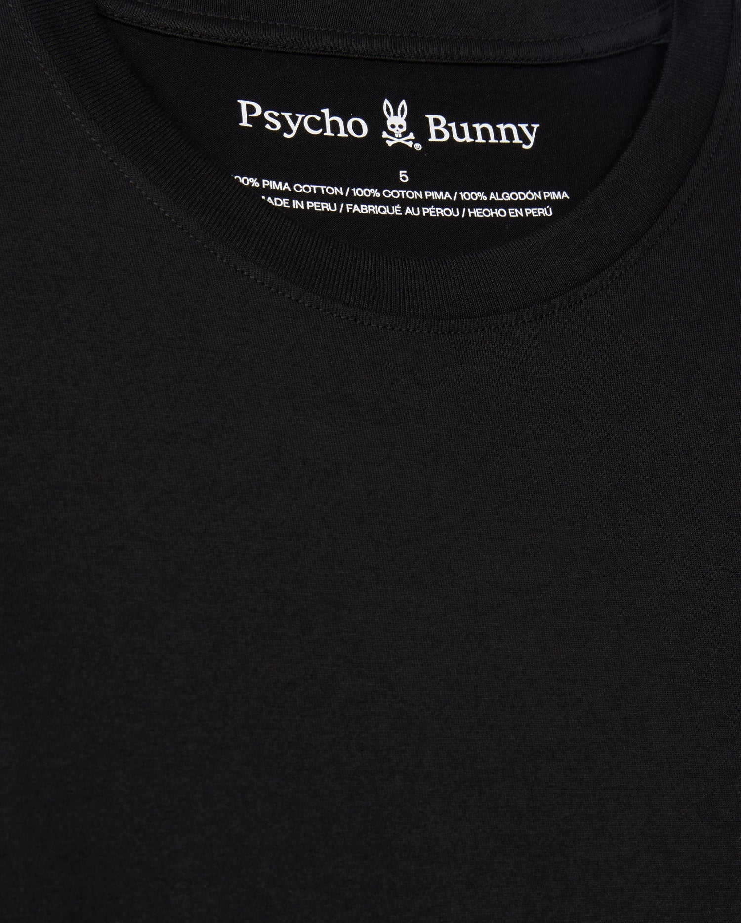 Here's a detailed description of the MENS JAMES PREMIUM CREW NECK TEE - B6U952D200 by Psycho Bunny: This close-up highlights the black, premium tee, showcasing "Psycho Bunny" printed at the inner neckline. Expertly crafted from 100% Pima cotton and made in Peru, it features a small bunny logo with crossbones neatly situated between "Psycho" and "Bunny." The text details are presented in multiple languages for an international appeal.