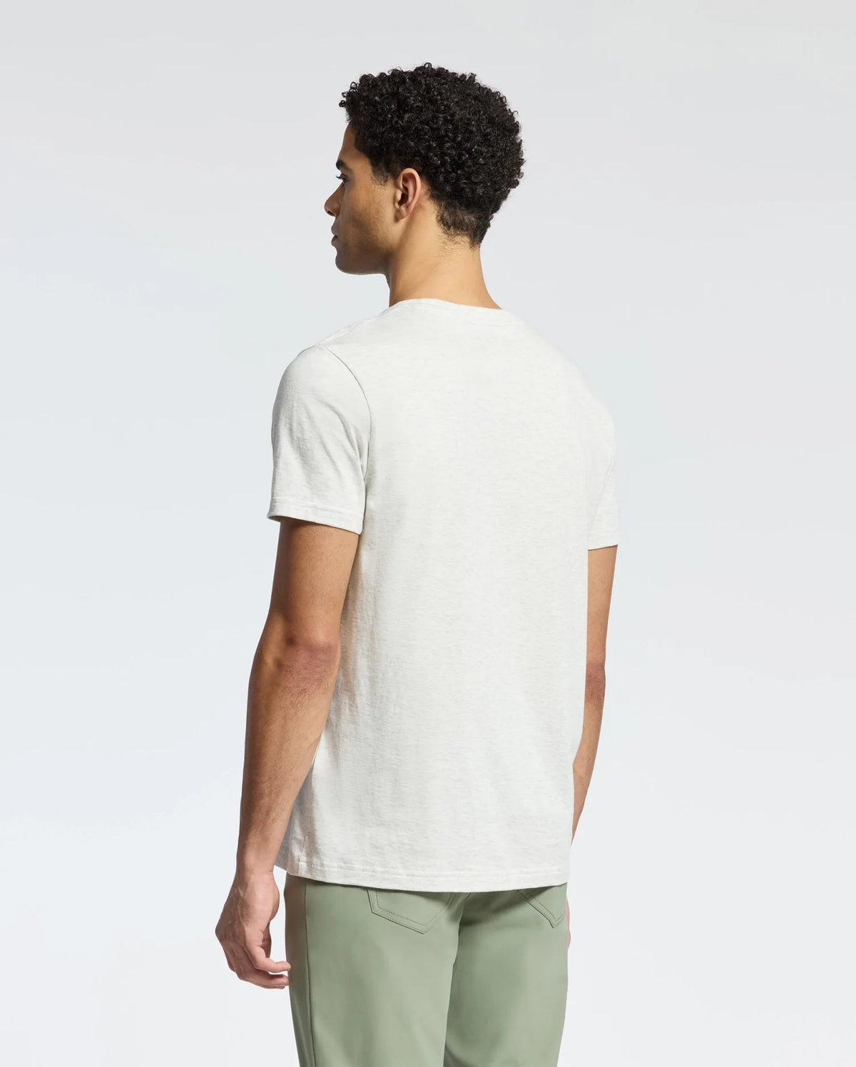 A person with short curly hair stands with their back to the camera, wearing a light gray Psycho Bunny MENS JAMES CREW NECK TEE (B6U952D200) and light green pants against a plain white background.