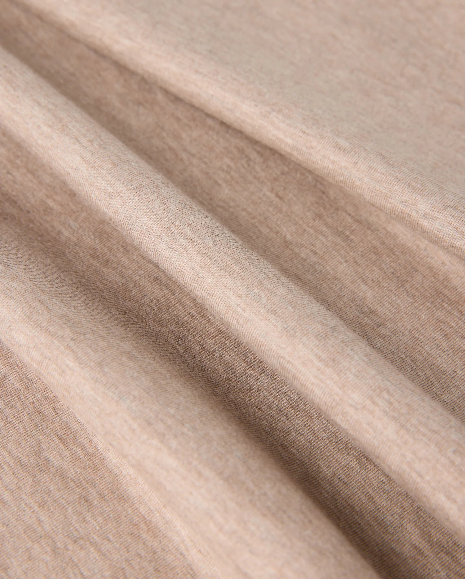 Close-up image of soft, light brown fabric with visible texture. The fabric appears to be folded in several smooth, gentle creases, showcasing its flexibility and softness. Made from premium Pima cotton, the material looks like it could be perfect for the MENS JAMES PREMIUM CREW NECK TEE - B6U952D200 by Psycho Bunny.