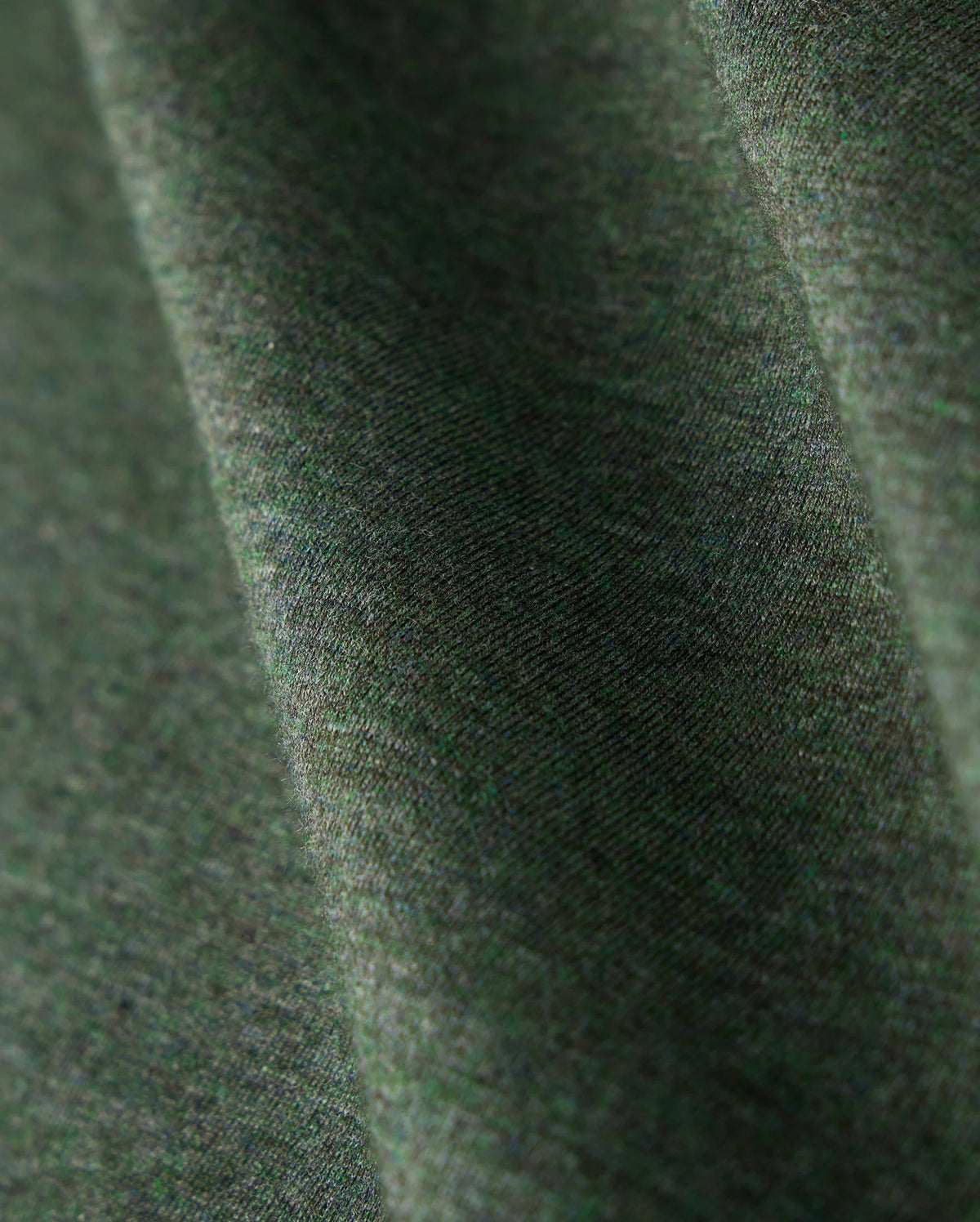 Close-up view of a green fabric with a slight texture and subtle heathered pattern. The premium Pima cotton material appears soft, captured with gentle folds that create a sense of depth. The lighting emphasizes the intricate weave, perfect for the stylish MENS JAMES PREMIUM CREW NECK TEE - B6U952D200 by Psycho Bunny.