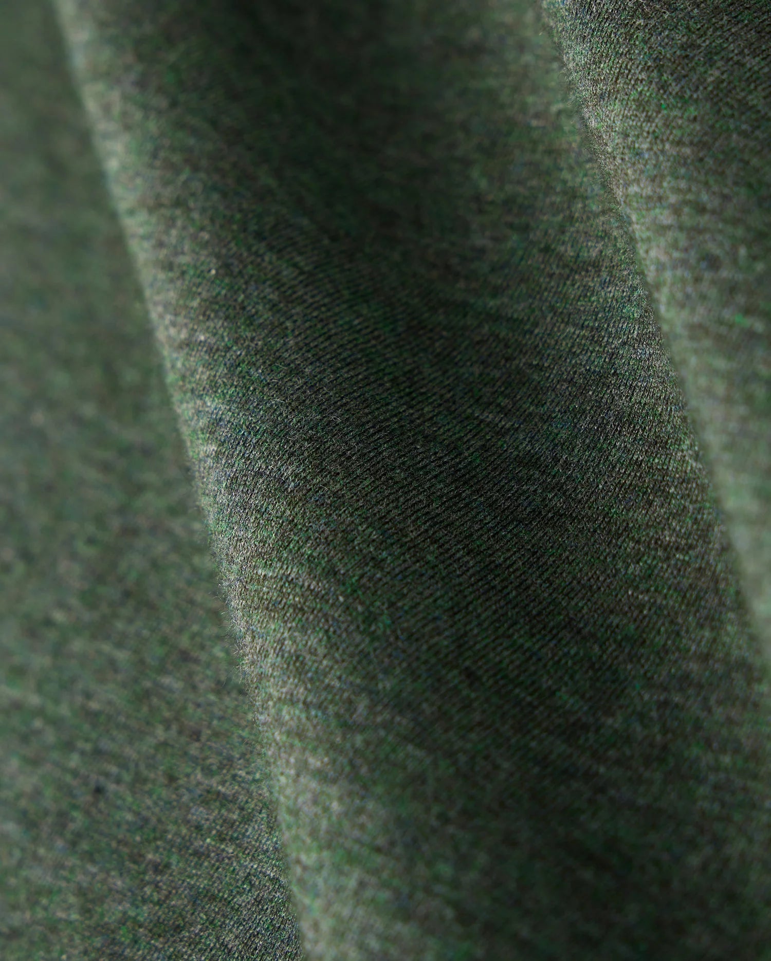 Close-up view of a green fabric with a slight texture and subtle heathered pattern. The premium Pima cotton material appears soft, captured with gentle folds that create a sense of depth. The lighting emphasizes the intricate weave, perfect for the stylish MENS JAMES PREMIUM CREW NECK TEE - B6U952D200 by Psycho Bunny.