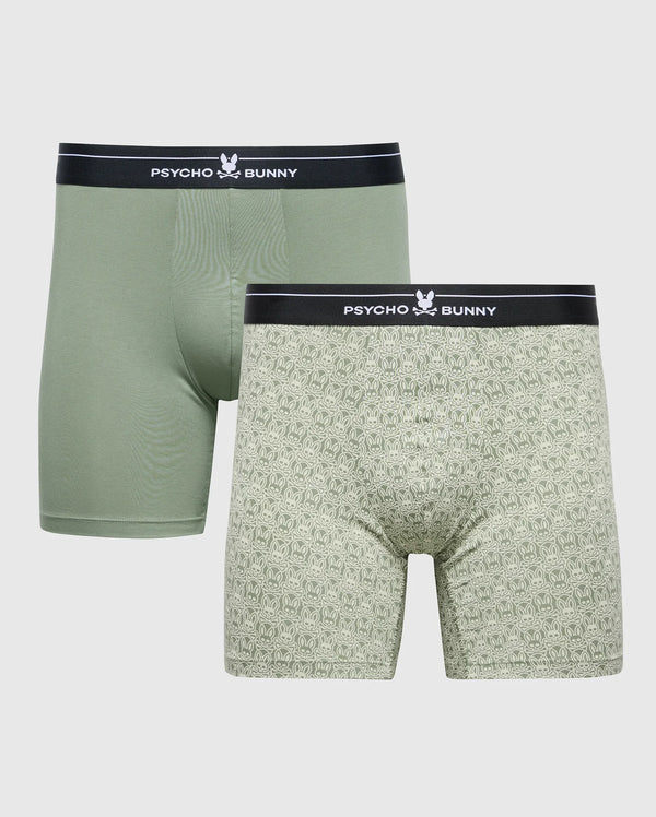 Two men's breathable boxers are set against a white backdrop. One is solid green, the other features a patterned design with small logos. Both have black waistbands displaying "Psycho Bunny" and a bunny logo in white, made from stretch Pima cotton for comfort. Product: MENS 2 PACK BOXER BRIEF - B6V481F200.