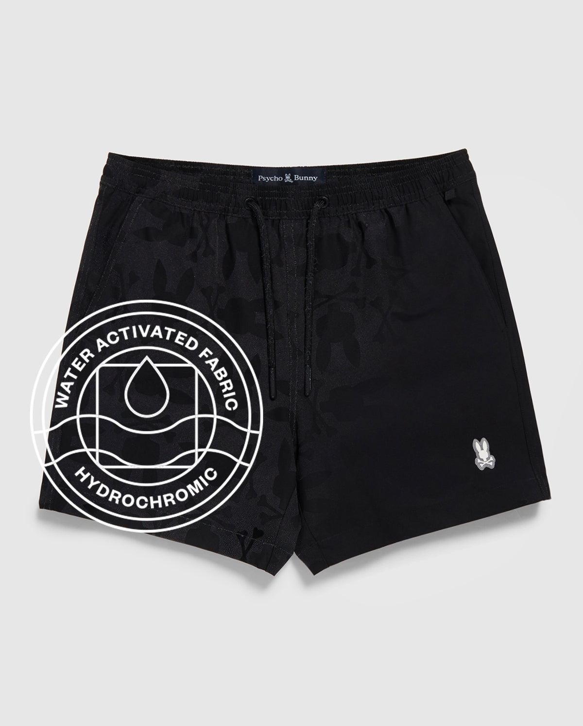 The Psycho Bunny MENS MALTA HYDROCHROMIC SWIM TRUNK (B6W321B2SW) features black fabric with a subtle bunny pattern, a small white logo on the left leg, and a "Water Activated Fabric Hydrochromic" circular graphic with a droplet icon.