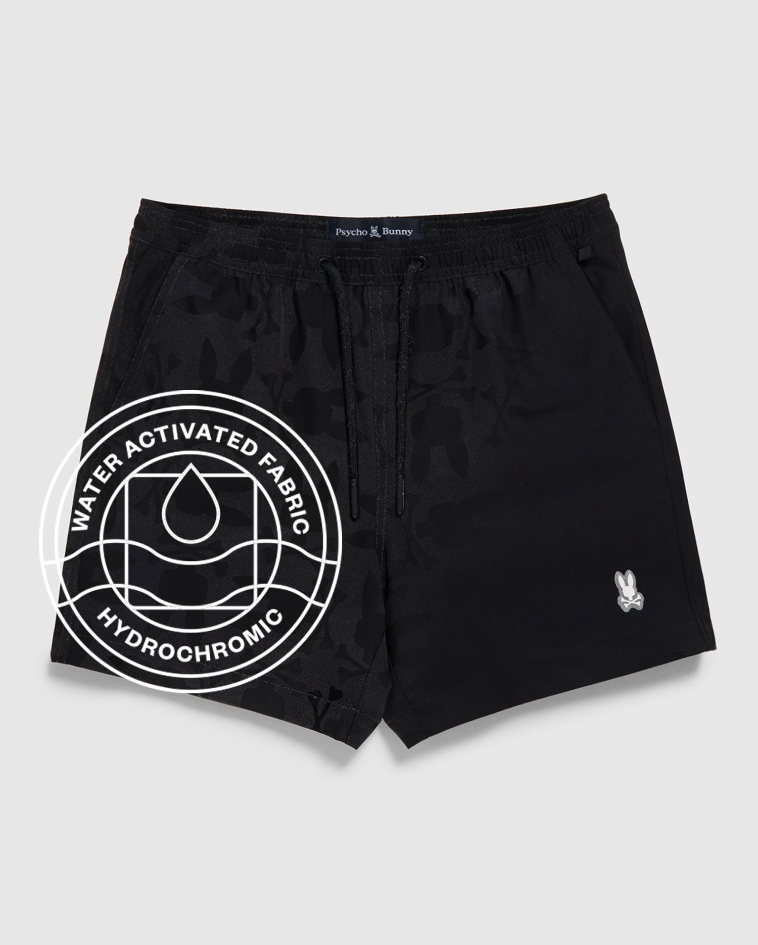 The Psycho Bunny MENS MALTA HYDROCHROMIC SWIM TRUNK (B6W321B2SW) features black fabric with a subtle bunny pattern, a small white logo on the left leg, and a "Water Activated Fabric Hydrochromic" circular graphic with a droplet icon.