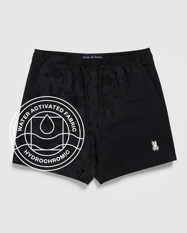 The Psycho Bunny MENS MALTA HYDROCHROMIC SWIM TRUNK (B6W321B2SW) features black fabric with a subtle bunny pattern, a small white logo on the left leg, and a "Water Activated Fabric Hydrochromic" circular graphic with a droplet icon.