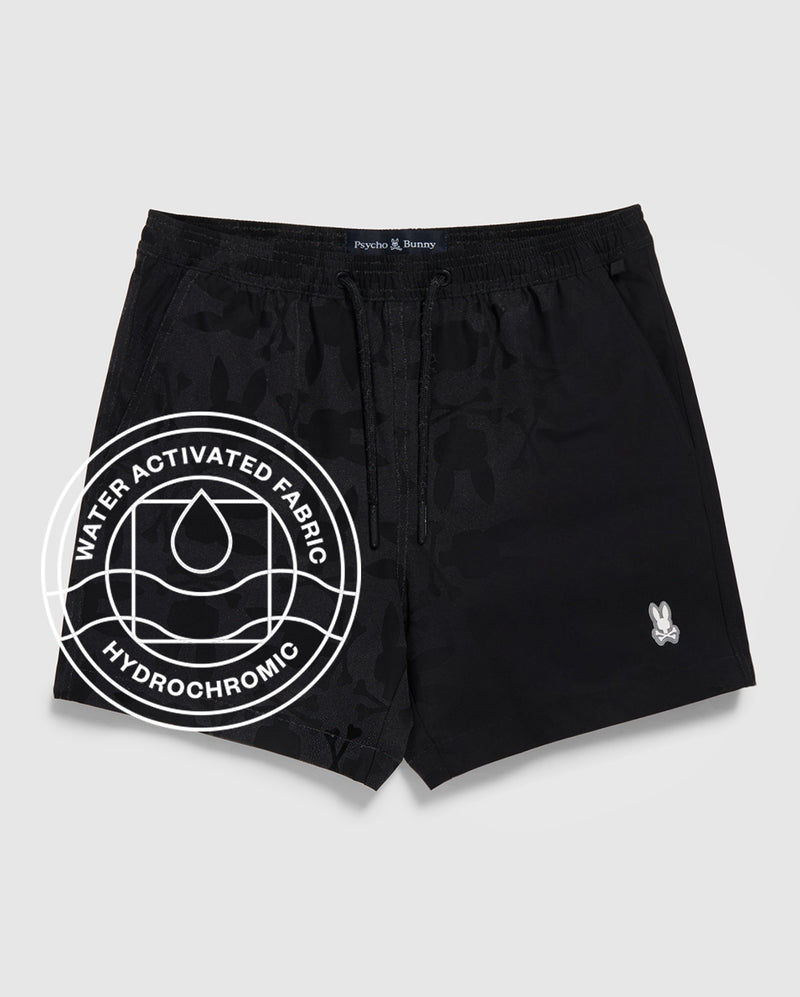 The Psycho Bunny MENS MALTA HYDROCHROMIC SWIM TRUNK (B6W321B2SW) features black fabric with a subtle bunny pattern, a small white logo on the left leg, and a "Water Activated Fabric Hydrochromic" circular graphic with a droplet icon.