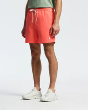 A person stands against a plain background wearing Psycho Bunny's MENS SAMOS HYDROCHROMIC PRINTED SWIM TRUNK - B6W453F200, pairing them with a light green shirt and white sneakers, perfect for a vibrant pool party.