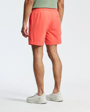 A person in a green shirt and light sneakers is standing, showcasing knee-length Psycho Bunny MENS SAMOS HYDROCHROMIC PRINTED SWIM TRUNK - B6W453F200, ideal for pool parties with an elastic waistband. The background is plain white.