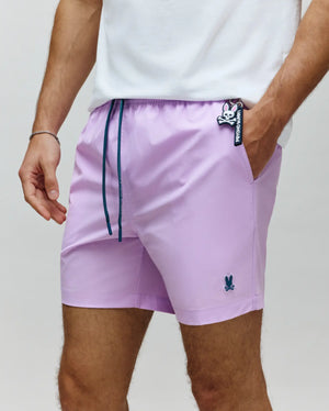 Mens Samos Hydrochromic Printed Swim Trunk in lavender, featuring a relaxed fit, smooth fabric, dark teal drawstring with Psycho Bunny text, small embroidered bunny skull on left leg, and a prominent bunny skull keychain.