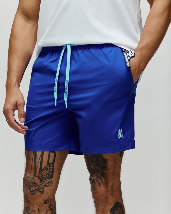 Mens Samos Hydrochromic Printed Swim Trunk, royal blue, relaxed fit, smooth fabric. Features aqua branded drawstrings, small embroidered bunny skull logo on left leg, and a Psycho Bunny keychain.