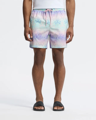 A person wears Psycho Bunny's MENS FORSTER BUNNY PRINTED SWIM TRUNK, a pastel-colored short with stars and bunnies featuring a pink drawstring, paired with a white shirt and black slide sandals against a plain white background. Their hands rest at their sides.