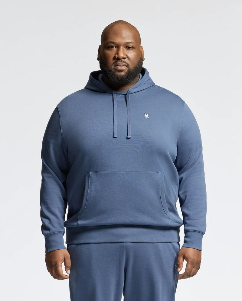 A man stands facing forward against a plain light background, wearing the Psycho Bunny MENS BIG AND TALL LEVY ESSENTIAL FLEECE HOODIE - B9H859D200 and matching blue cotton sweatpants.