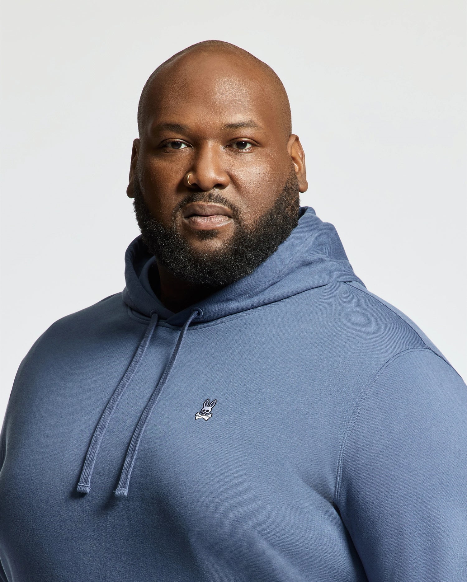 A man with a bald head and full beard confidently models the Psycho Bunny MENS BIG AND TALL LEVY ESSENTIAL FLEECE HOODIE - B9H859D200, made from 100% cotton, against a plain light background.