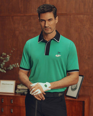 Indoors, a man holds a golf club, wearing an MT0100004 green Psycho Bunny polo made from soft Pima cotton and a white glove. A wooden wall with shelves displaying a plant and framed pictures completes his stylish look.