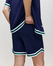 Teen | A person in Psycho Bunny's KIDS BASIL TAPED SHORT (KB0900003) and a navy cotton-modal shirt with white and green striped trim stands confidently, showcasing a sporty, casual style.