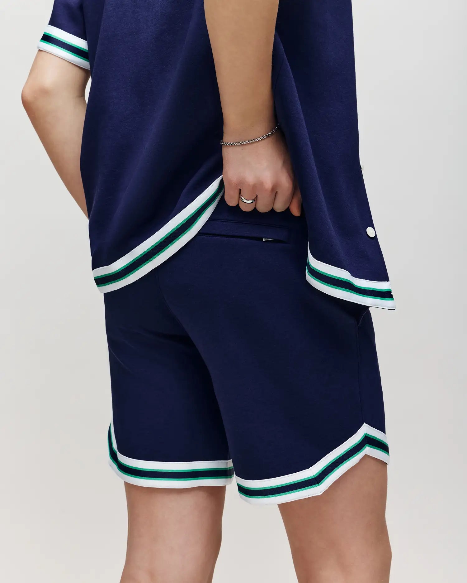 Teen | A person in Psycho Bunny's KIDS BASIL TAPED SHORT (KB0900003) and a navy cotton-modal shirt with white and green striped trim stands confidently, showcasing a sporty, casual style.