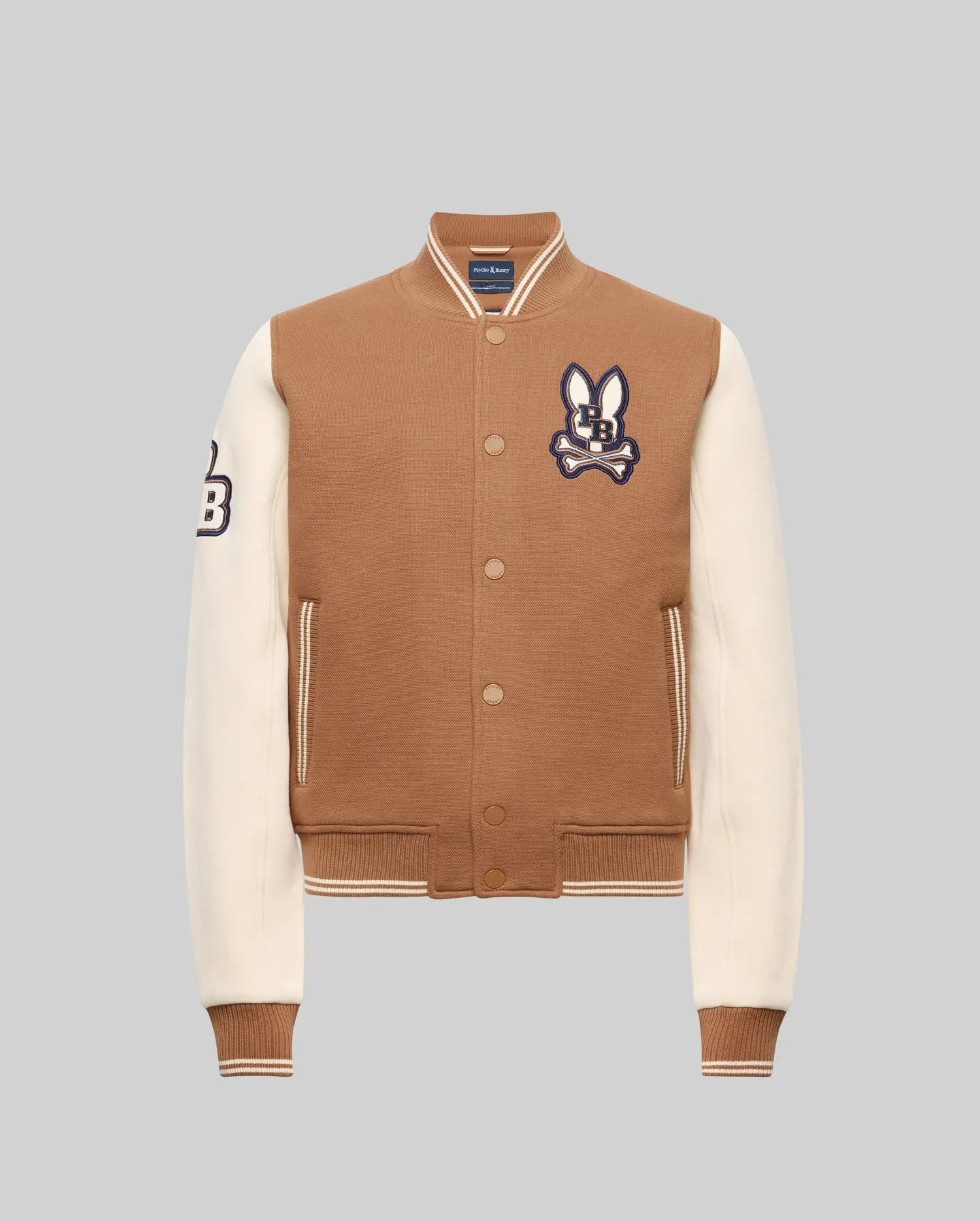 The Psycho Bunny KIDS WADE KNIT BOMBER (KO1100001) is a brown varsity jacket with cream sleeves, ribbed cuffs and hem, bunny patch on the chest, "B" patch on the sleeve, front pockets, and snap button closures. Made from a premium cotton blend.