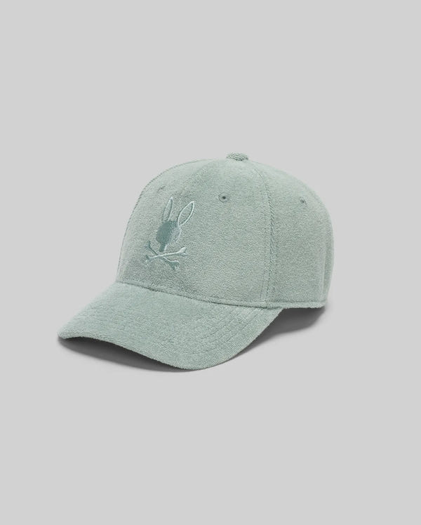 The Psycho Bunny KIDS KELVIN TOWEL TERRY BASEBALL CAP (KO1500007) is a mint green, soft terry cloth cap with an embroidered Bunny head above crossed lines on the front, shown against a plain light gray background.
